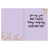 The Queen Birthday Card by Natalie Henry Charles features a light purple background with orange, yellow, and pink flowers. The black handwritten text says: giving you your flowers today & every day. ENJOY YOUR DAY! Printed in the USA.