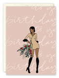 The Amy Slaughter Its Your Birthday Card features a woman in a short beige dress with black boots and flowers, “it’s your birthday” script on light pink, printed in the USA on high-quality recycled paper.