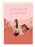 The She Believed Congrats Card by Amy Slaughter features an illustrated woman in a long dress on a patterned rug, candles around her, with the phrase She believed she could so she tried and tried on a pink background. USA made, printed on recycled paper.