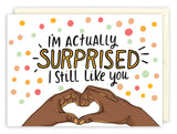 The Surprised I Still Like You Anniversary Card by Andrea Williams features colorful dots, playful text, and two brown hands forming a heart. Printed on recycled paper, its perfect for anniversaries or any day you want to share some love.
