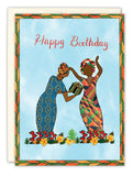 Two women in patterned dresses stand on grass and flowers, exchanging a gift. The All The Love Birthday Card by Cherrymae Golston is printed on recycled paper, with geometric borders and “Happy Birthday” in red at the top.