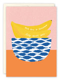 The Bananas Anniversary Card by Lauren-Ashley Barnes features two bananas in a blue and white bowl with Our love is bananas, lets never split on a playful pink background—perfect for wishing a colorful, happy anniversary.